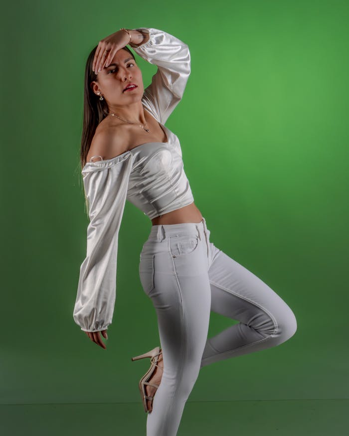 Fashionable woman in a dynamic pose, wearing a white outfit and posing against a green studio background.